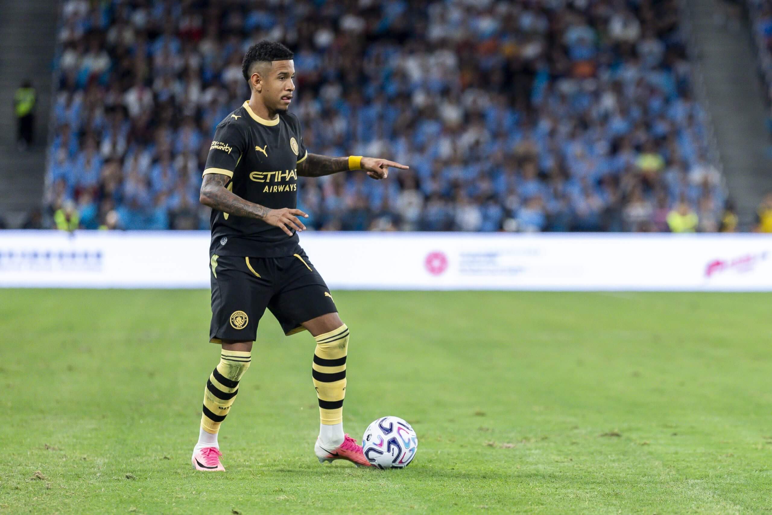 Savinho dribbling the ball off his left foot in a black Man City kit