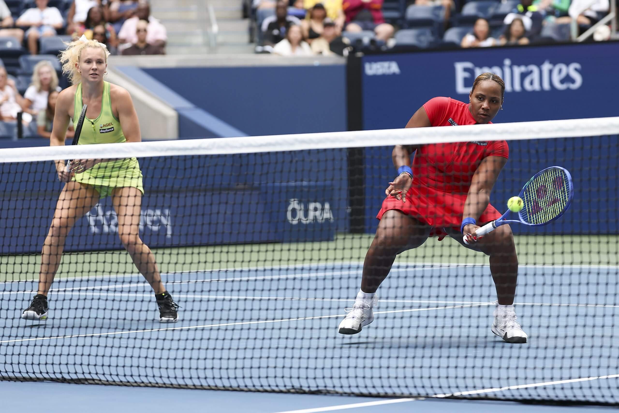 Kateřina Siniaková glances left in her ready stance while partner Taylor Townsend delivers a left‑handed forehand volley.
